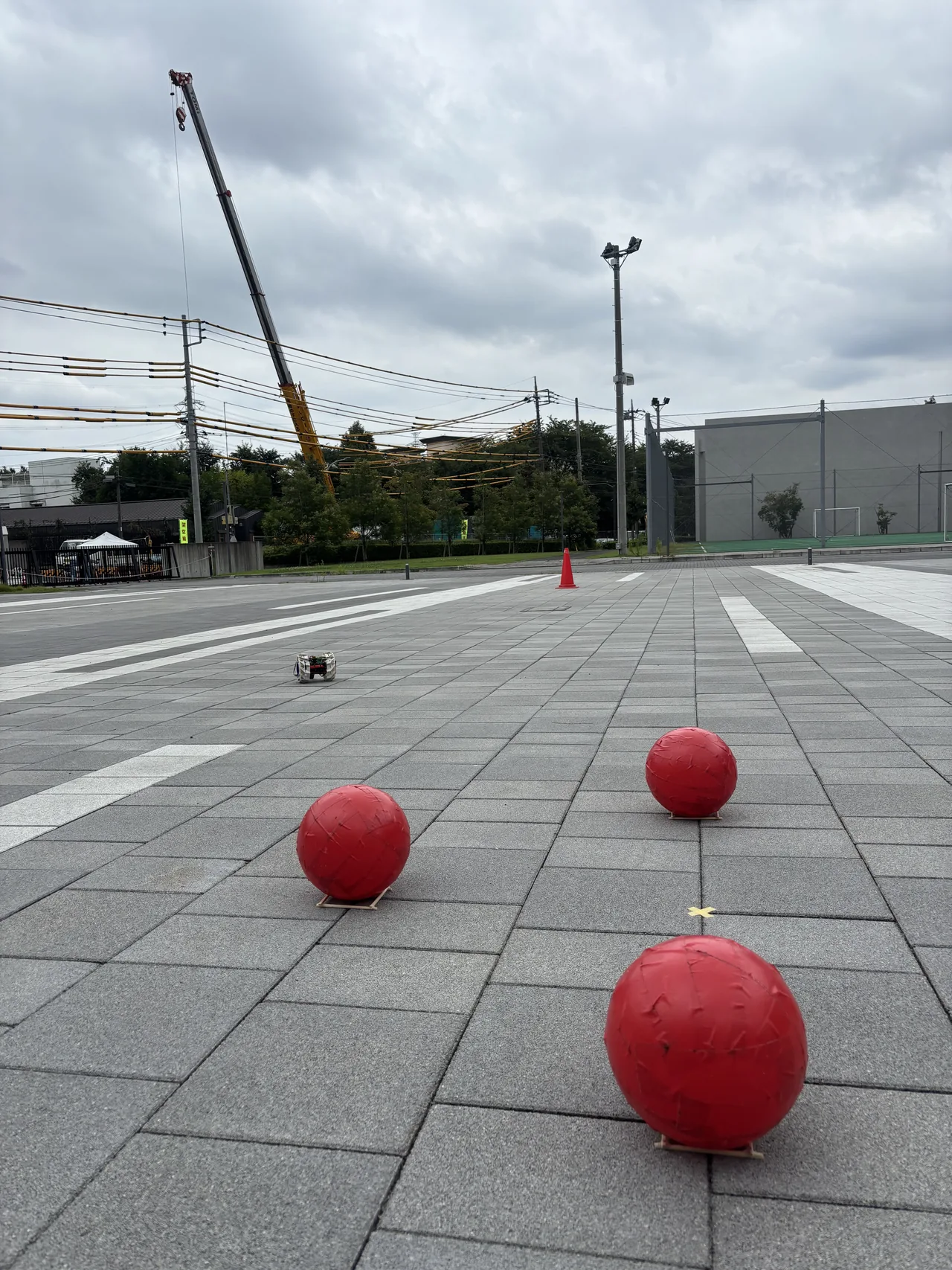 Un prototipo CanSat en un curso pavimentado con marcadores rojos y una grúa en el fondo.